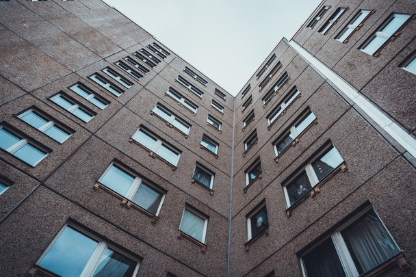 Low Angle Architectural Exterior of Mid Rise Residential Apartment Building with Brown Stone Facade and Repeating Windows Diminishing Upwards Toward Overcast Sky - Photo, Image