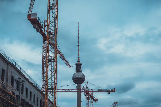 Κοιτάζοντας ψηλά στην κατασκευή γερανοί Κτίριο Νέα ανάπτυξη με θέα την τηλεόραση Transmission Tower στο παρασκήνιο Framed by Heavy Dark Storm Σύννεφα στο Βερολίνο, Γερμανία - Φωτογραφία, εικόνα