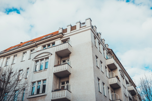 Extérieur architectural à faible angle du coin de l'immeuble résidentiel moderne à faible hauteur avec petits balcons et façade blanche, encadré par ciel nuageux et arbres nus à Berlin, Allemagne
 - Photo, image