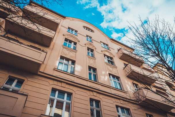 Nízký úhel Architektonický Exteriér moderního luxusního bytového domu s dlouhými balkony a klasickými dekorativními prvky, obklopen holými stromy a modrým nebem v Berlíně, Německo - Fotografie, Obrázek