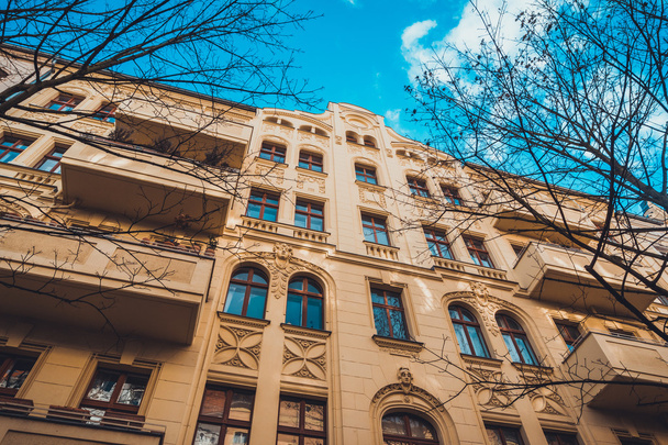 Nízký úhel Architektonický Exteriér moderního luxusního bytového domu s dlouhými balkony a klasickými dekorativními prvky, obklopen holými stromy a modrým nebem v Berlíně, Německo - Fotografie, Obrázek