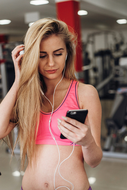 Blonde with a phone  at the gym. Listening to music - Photo, Image