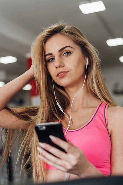 Blonde with a phone  at the gym. Listening to music - Фото, изображение