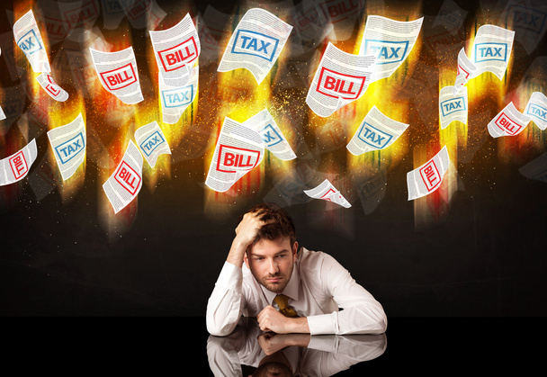 Depressed businessman sitting under burning tax and bill papers - Foto, Imagen