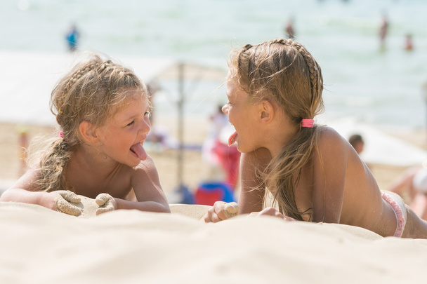 二人の幸せな小さな女の子は砂浜でお互いの舌を示しています - 写真・画像