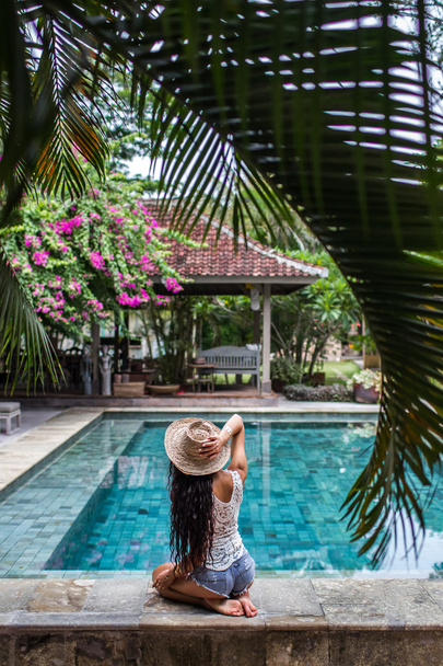 Jeune femme mince en jeans short relaxant près de la piscine avec chapeau de paille
 - Photo, image