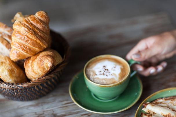 Mulher mão segurando xícara de cappuccino aroma no café da manhã com panquecas
 - Foto, Imagem