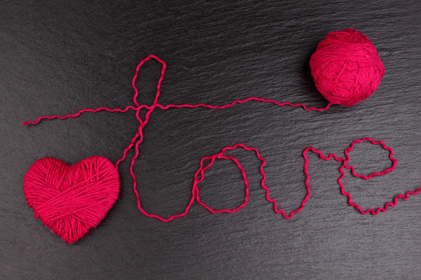 rote Klammern in Herzform mit dem Wort "Liebe" aus Wolle auf schwarzem Hintergrund - Foto, Bild