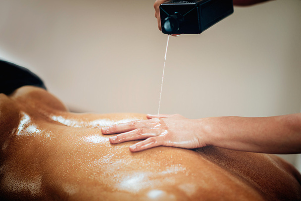 Therapeut schüttet Massageöl auf den Rücken des Klienten - Foto, Bild