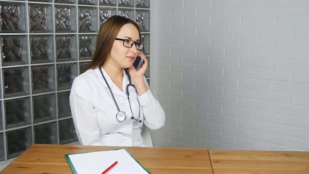 Kobieta lekarz siedzi w swoim biurze i korzystanie smartphone - Materiał filmowy, wideo