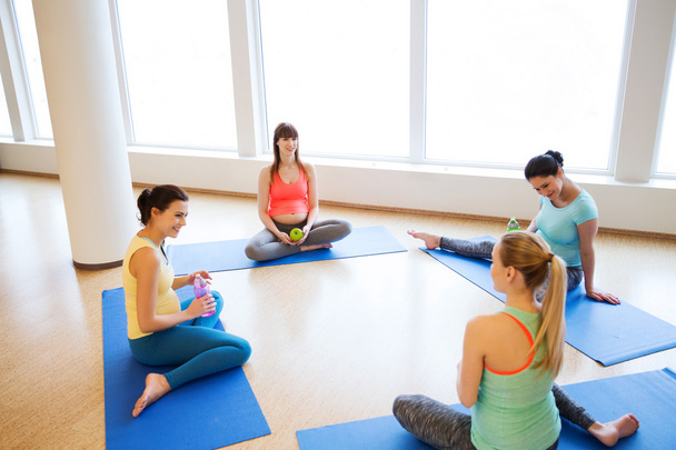 happy pregnant women sitting on mats in gym - Foto, immagini