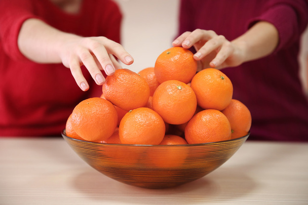 Woman taking tangerines from the bowl - Фото, изображение