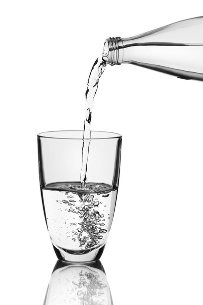 Pouring water from bottle into glass over grey background - Foto, Bild