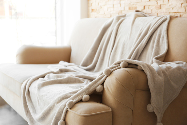 Gray blanket draped over a beige couch - 写真・画像