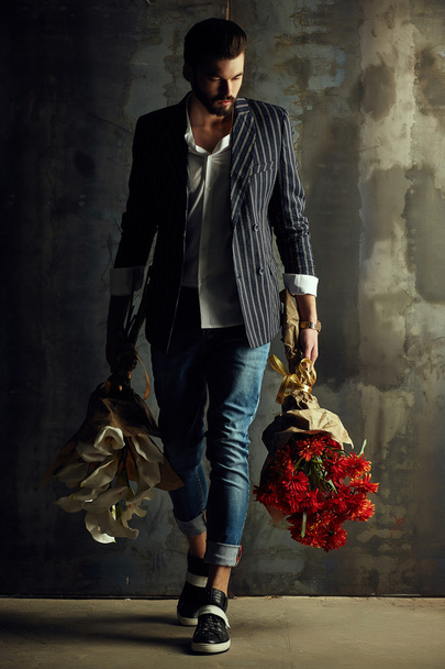 Handsome young man in smart jacket with bouquet of flowers  poses in front of the  wall - Фото, зображення
