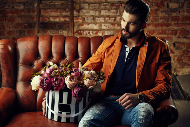 Handsome young man in smart jacket with bouquet of flowers  poses in front of the  wall - Foto, immagini