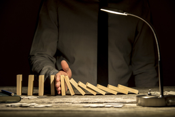 Vooraanzicht van zakenman stoppen vallende dominos met zijn hand - Foto, afbeelding