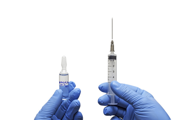 Medical gloved hand holding syringe with a bead of liquid emerging testing the function of the syringe - Foto, imagen