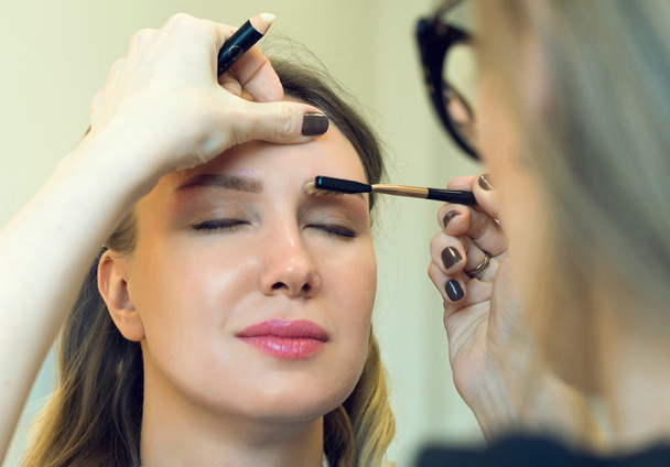 Make-up artist combing eyebrow on model's face. - Фото, изображение