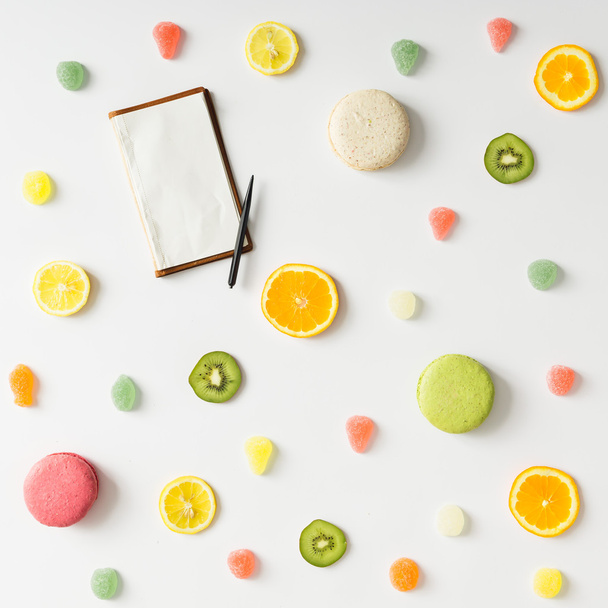 Colorful bright fruit pattern with notebook and sweets on white  - Photo, image