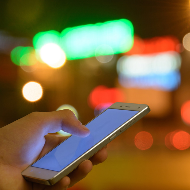 Ο άνθρωπος οθόνη αφής κινητό τηλέφωνο, νύχτα φως bokeh φόντο - Φωτογραφία, εικόνα