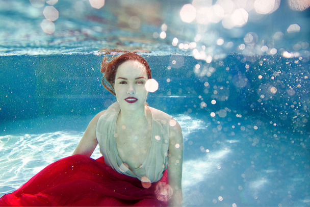 Χαμογελαστά νέοι όμορφη λευκή γυναίκα στο φόρεμα κάτω από το νερό στην πισίνα - Φωτογραφία, εικόνα