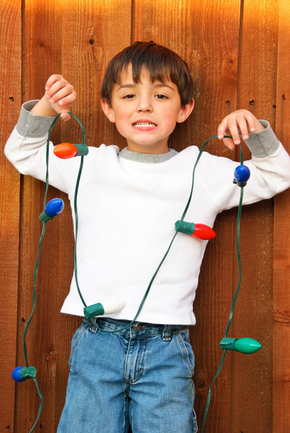 Adorable little boy holding Christmas lights with funny smile. - Photo, Image