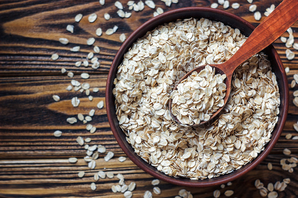 Food. Oatmeal on the table. Dry rolled oat flakes oatmeal in brown bowl on old wooden table. - Photo, Image