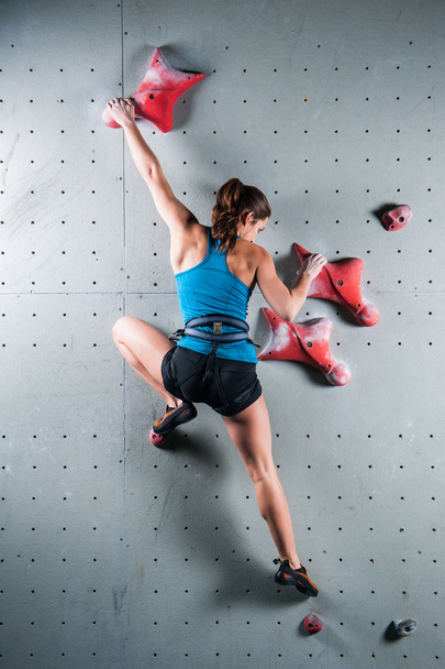 Young woman climbing up on practice wall in gym - Foto, afbeelding