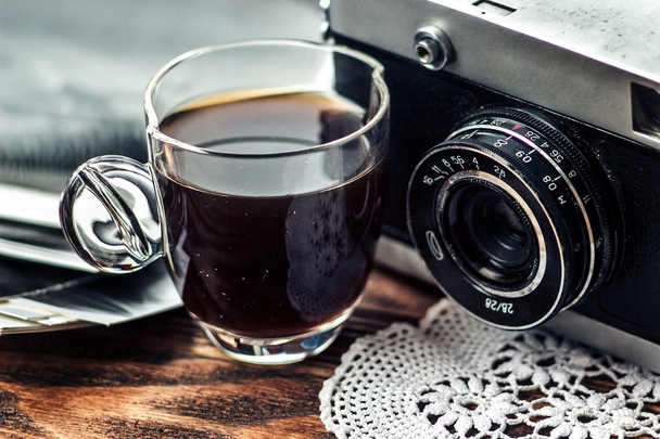 Close up photo of old, vintage camera lens with cap of coffee and black and white photos over wooden table. Nostalgic holidays background. Memories concept. Image is retro filtered. Selective focus - Φωτογραφία, εικόνα