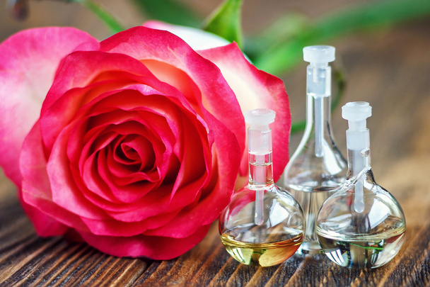 Essential oil in glass bottle with rose flowers on wooden background. Small bottles of perfume. Beauty treatment. Spa concept. Selective focus. - Photo, Image