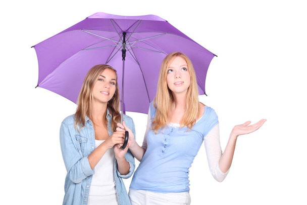 Two young blonde women under a umbrella, one of them is looking up and holding out one's hand - Fotografie, Obrázek