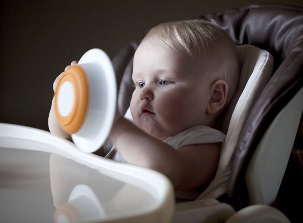 Baby boy sitting at a table for feeding with an empty plate - Foto, Imagen