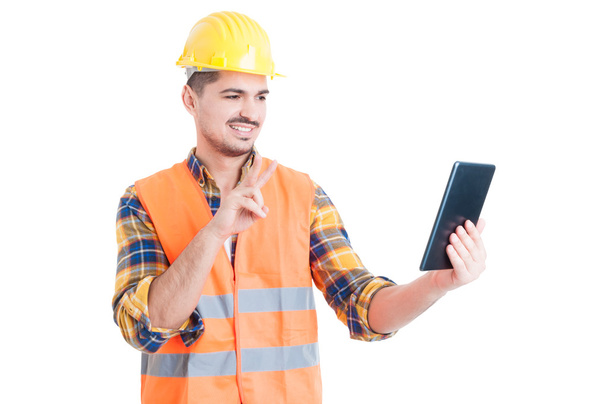 Smiling constructor using tablet and showing peace or victory ge - 写真・画像