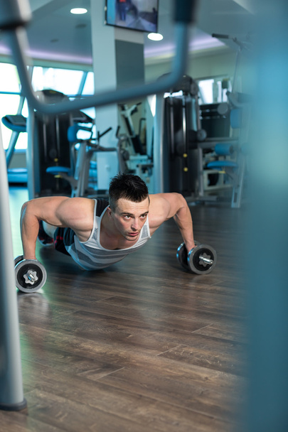 М'язистий чоловік робить штовхання на гантелі в спортзалі. Потужний чоловік e
 - Фото, зображення
