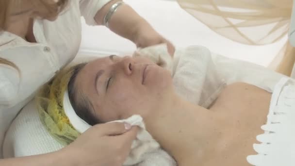 Женщина-косметолог вытирает женщине лицо и шею салфетками в салоне красоты
. - Кадры, видео