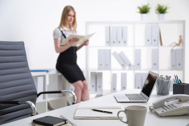 Office table, blurred blonde businesswoman standing at table at background. Office. Concept of work. - Foto, imagen