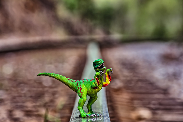 Green Velociraptor dinosaur walking on rail railroad tracks - Photo, Image