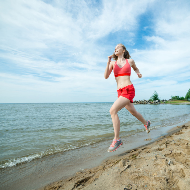 Fiatal hölgy futás a napsütéses nyári homokos strandon. Edzés. Jog - Fotó, kép