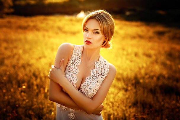 Modefoto der schönen jungen Mädchen mit blonden Haaren trägt luxuriöse beige Kleid bei Sonnenuntergang. - Foto, Bild