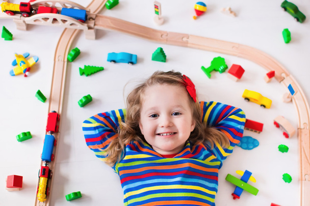 Маленькая девочка играет с деревянными поездами
 - Фото, изображение