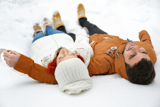 Young couple lying on the snow outdoors in winter - Фото, зображення