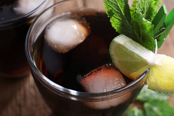 Glass of cola with ice, mint and lime on wooden table background, closeup - Photo, image