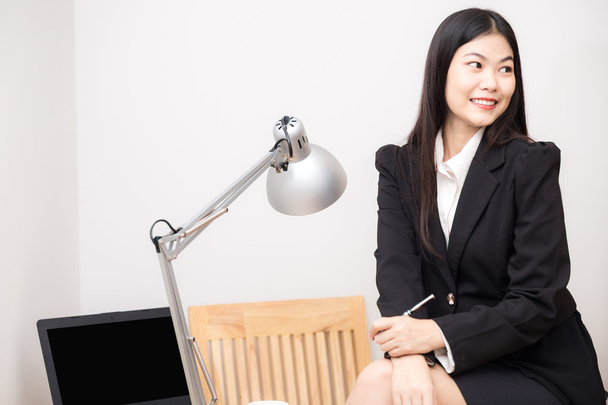 Портрет щасливої азіатської бізнес-леді, що сидить на її робочому місці в офісі з ноутбуком
 - Фото, зображення