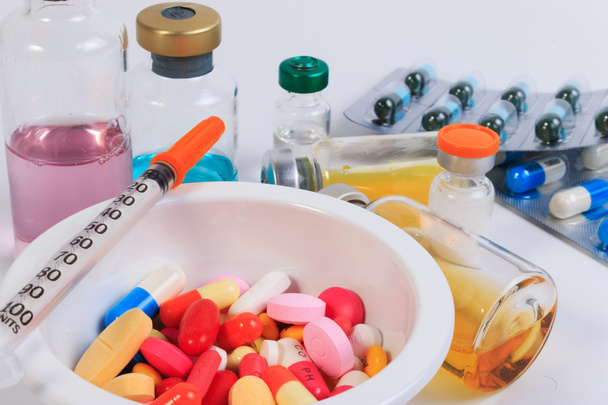 Багато кольорових таблеток, капсул і шприца в чашці з ложкою і пляшкою вакцини
. - Фото, зображення