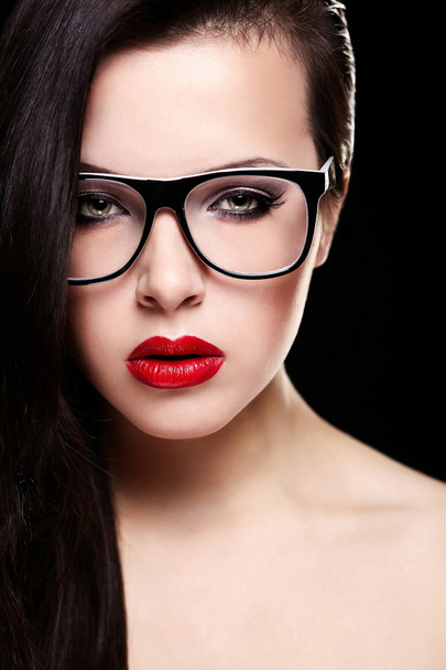 Fashion portrait of beautiful brunette girl model in glasses with birght makeup red lips. Clean skin. Isolated on black - Foto, Bild