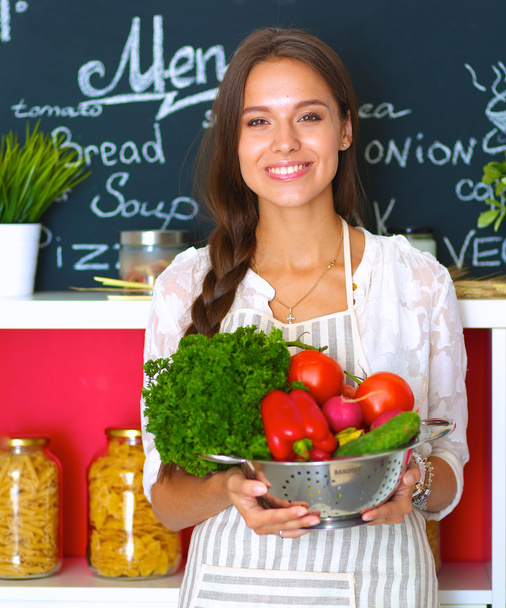 Mosolygó fiatal nő gazdaság zöldség áll a konyhában - Fotó, kép
