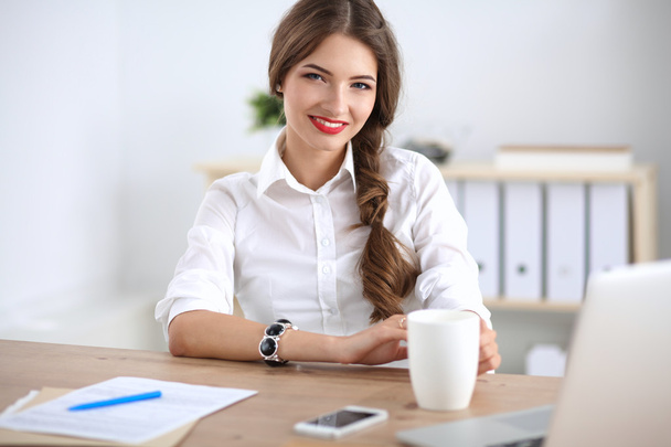 Attractive businesswoman sitting  on desk in the office - Фото, изображение