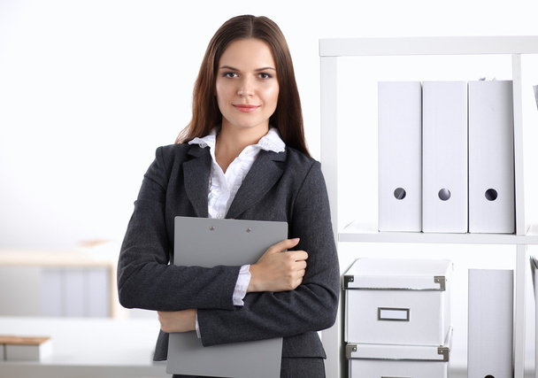 Attractive young businesswoman standing near desk with folder in the office - Foto, immagini