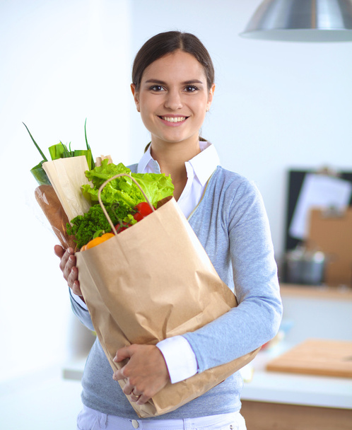 Jonge vrouw met boodschappentas met groenten.Staande in de keuken - Foto, afbeelding